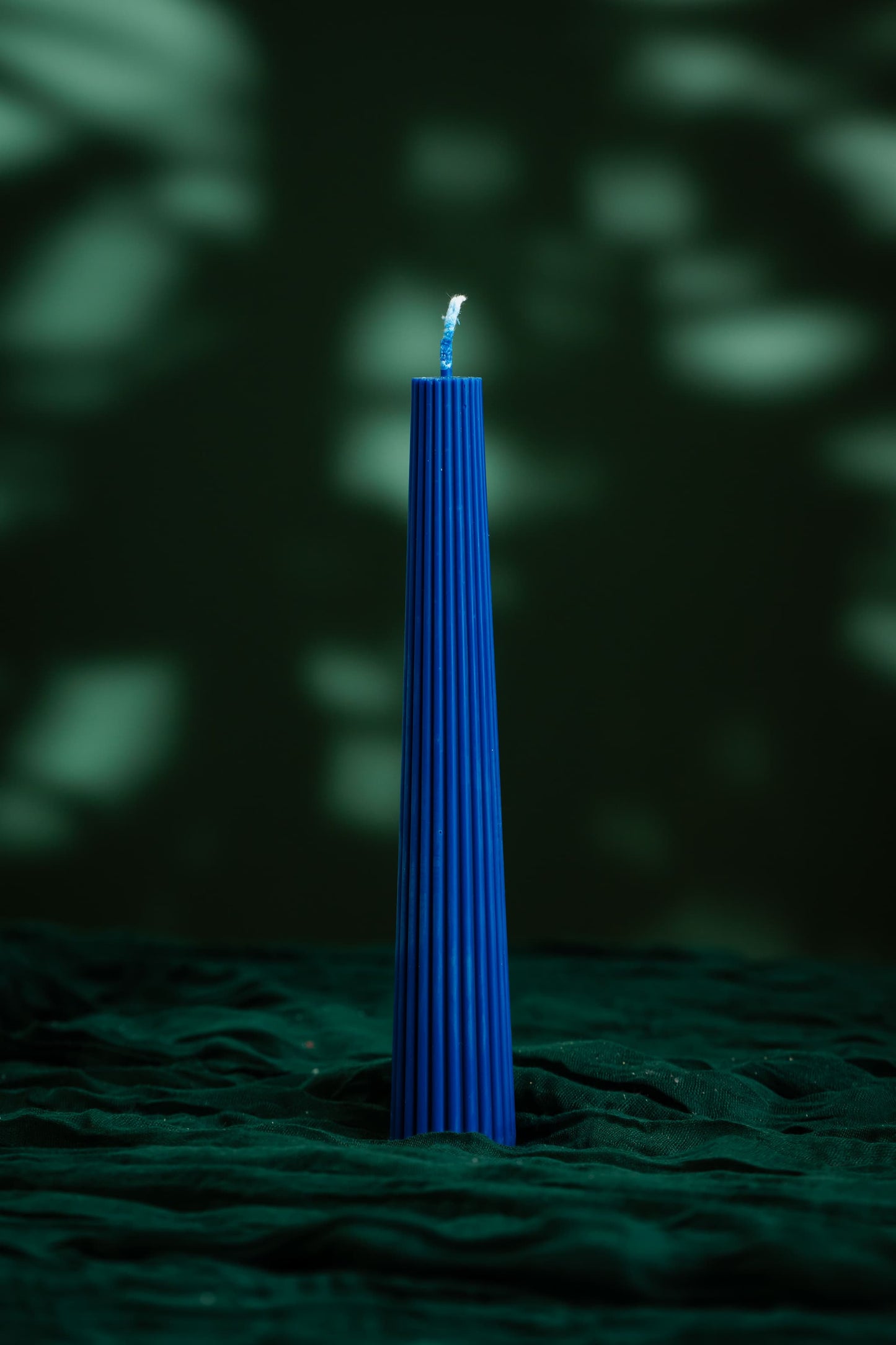 Blue candle on a textured green surface with a dark background