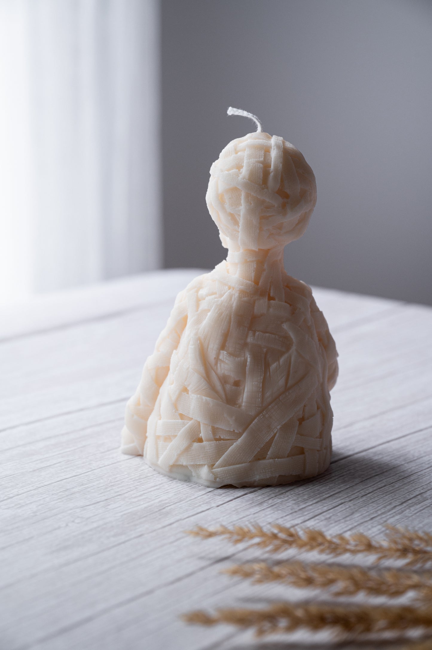 Candle shaped like a person wrapped in yarn on a wooden surface with a blurred background