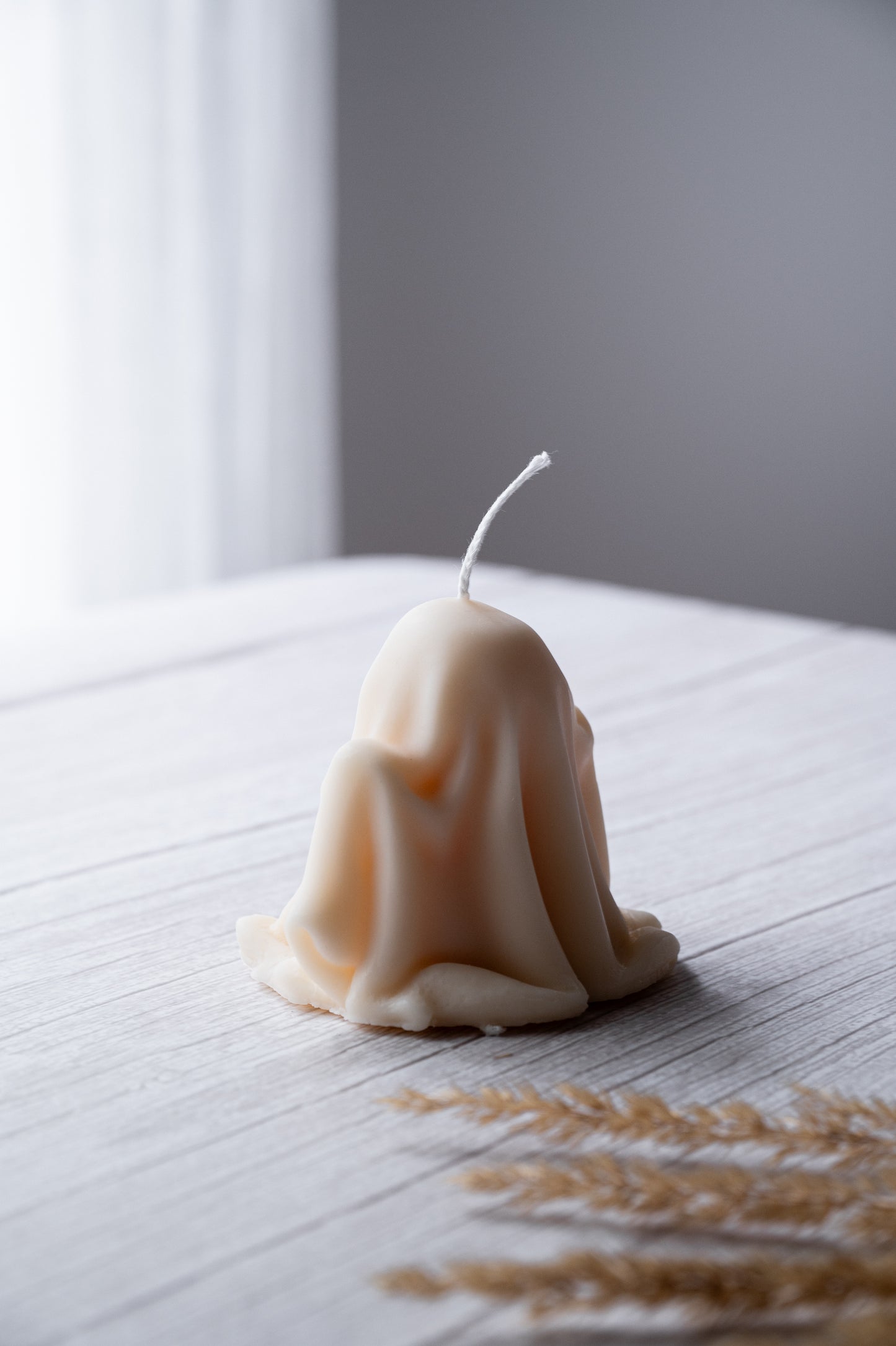 Candle shaped like a ghost on a wooden surface with a blurred background