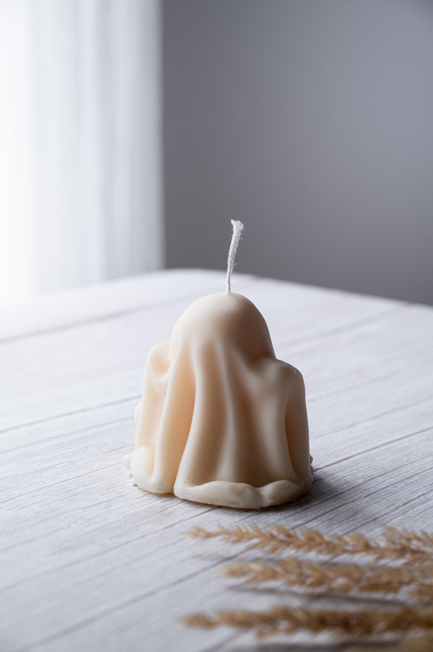 Candle shaped like a ghost on a wooden surface with a blurred background
