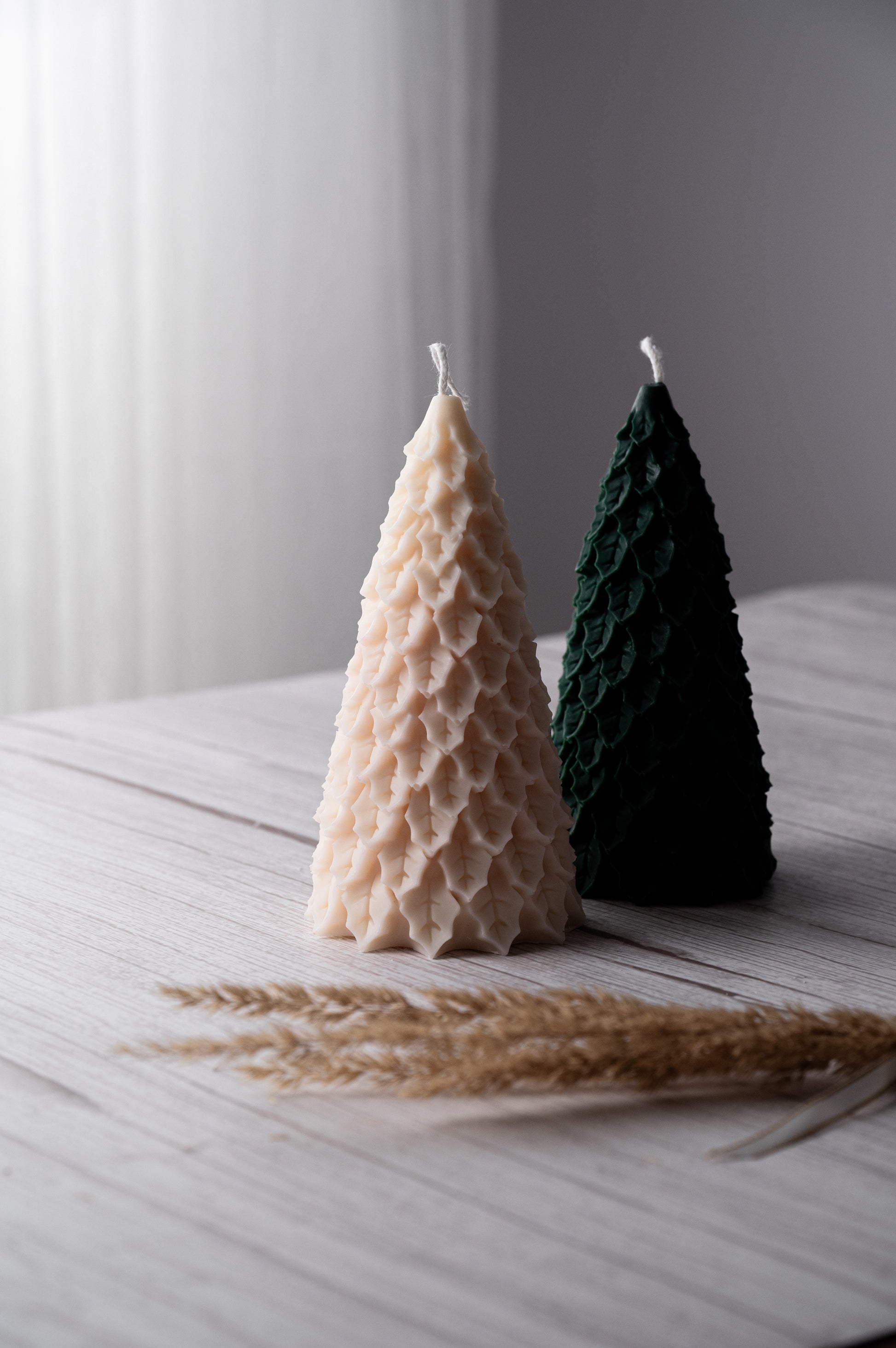 Two cone-shaped candles, one beige and one green, on a light wooden surface with a blurred background.