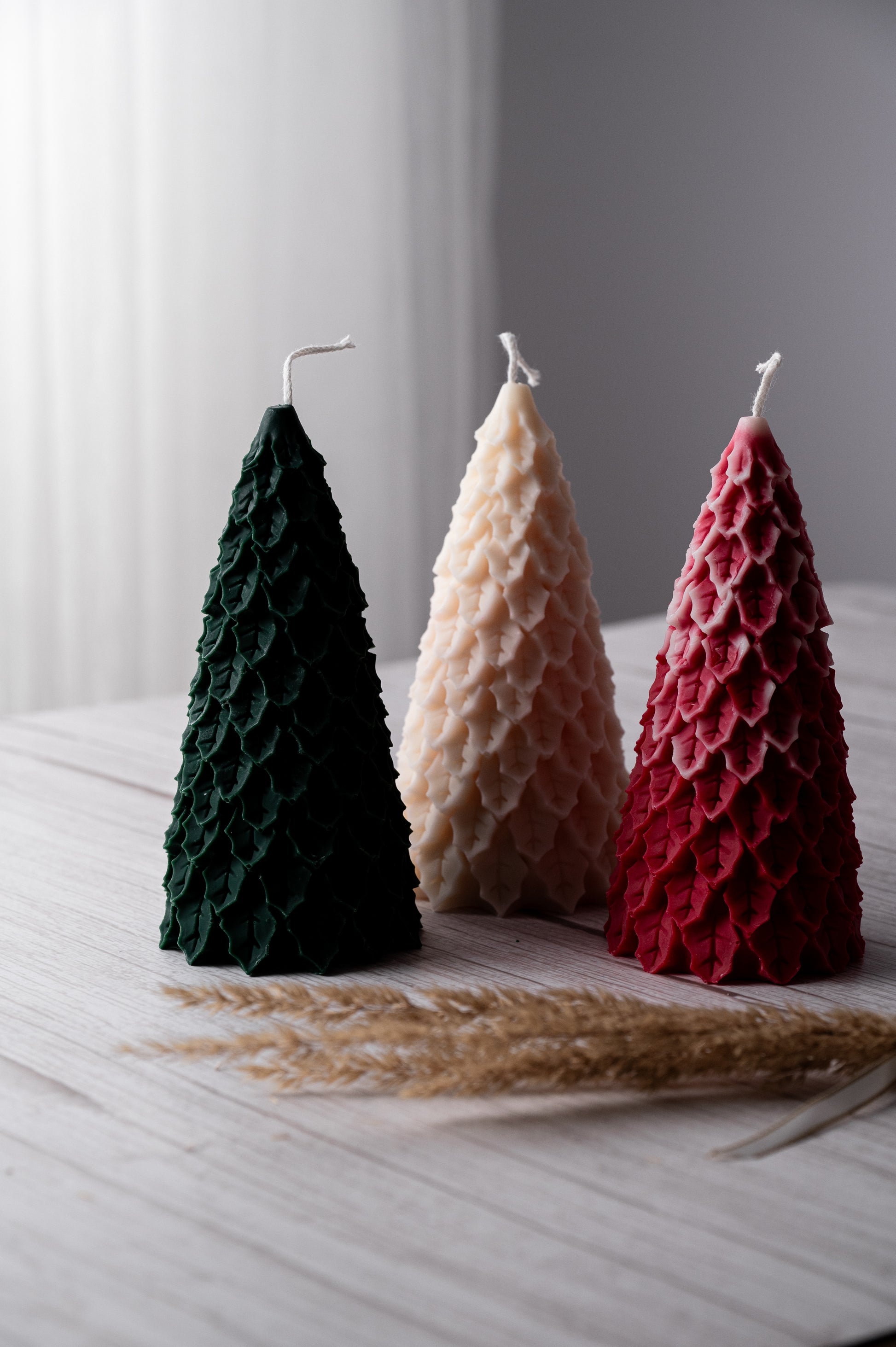 Three textured candles in green, beige, and red on a light surface with a blurred background