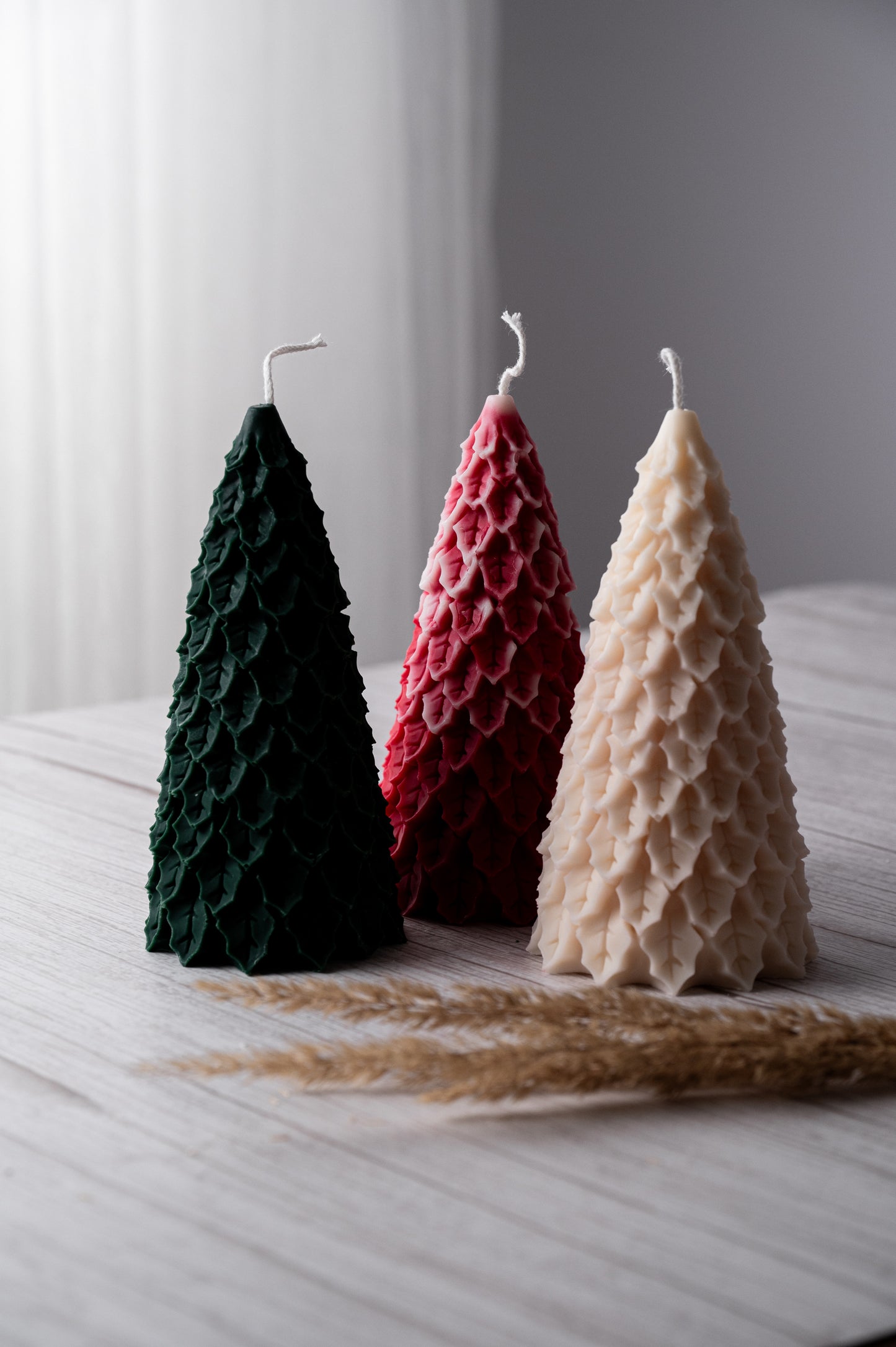 Three tree-shaped candles in green, red, and beige on a light surface with a blurred background.