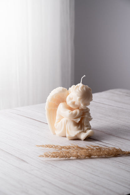 A candle with an angel statue design on it, placed on a wooden surface with some wax dripping down the side.