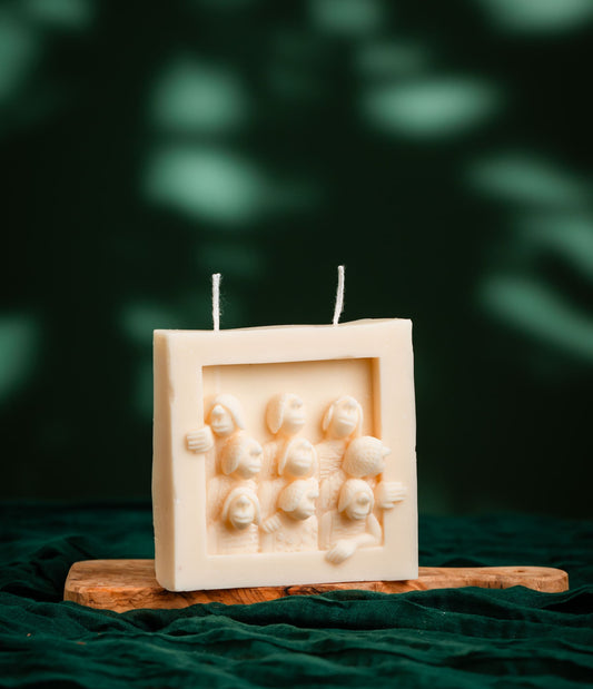 Square white candle with decorative elements on a wooden stand against a dark green background