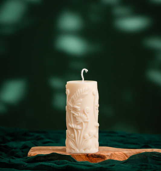 Decorative candle with intricate design on a wooden board against a dark green background