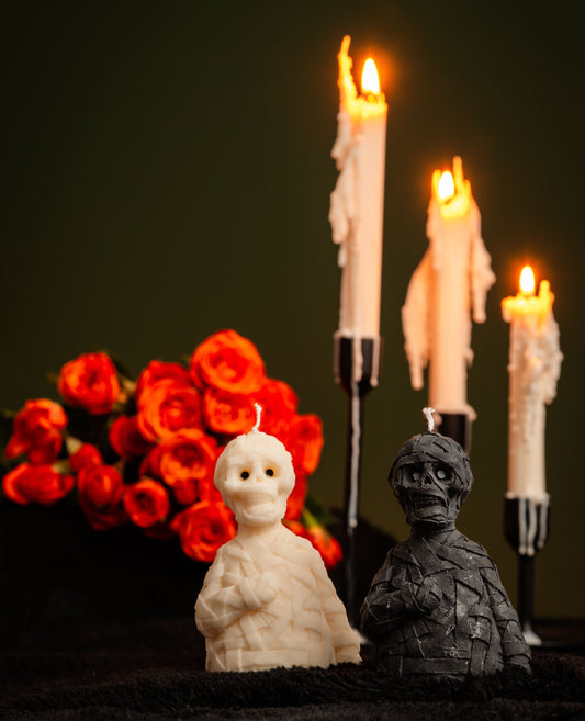 Two ghost-shaped candles with a bouquet of red roses and lit candles in the background.