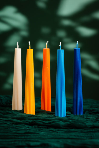 Five colorful candles of different heights on a dark green leafy background