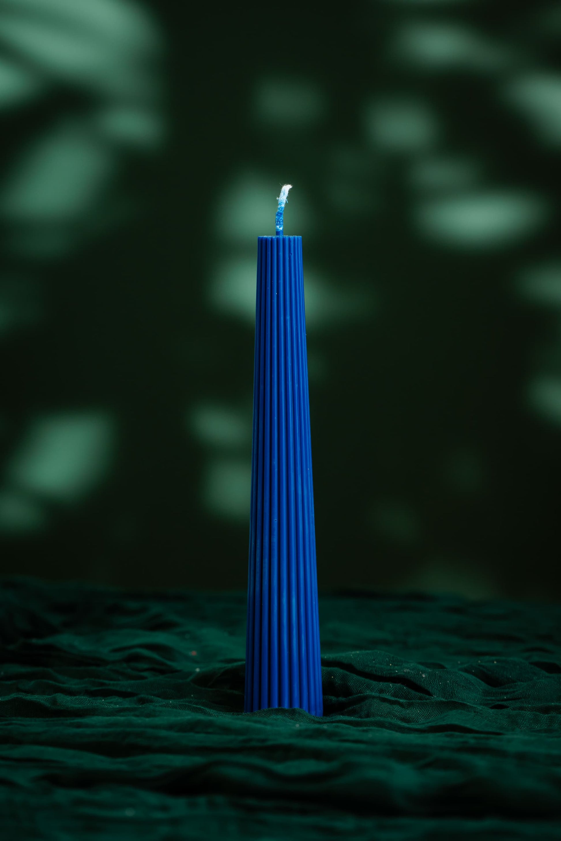 Blue candle on a textured green surface with a dark background