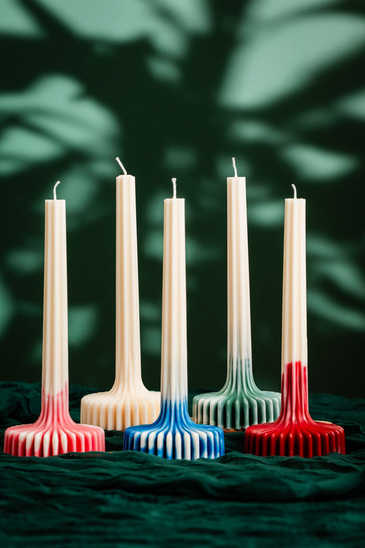 Set of five decorative candles with gradient colors against a dark green leafy background