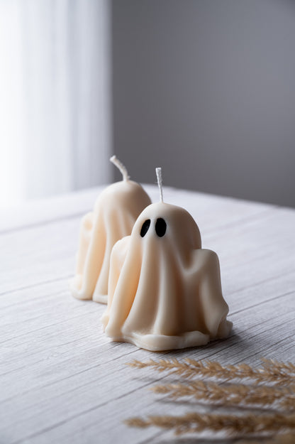 Three ghost-shaped candles on a light surface with a blurred background