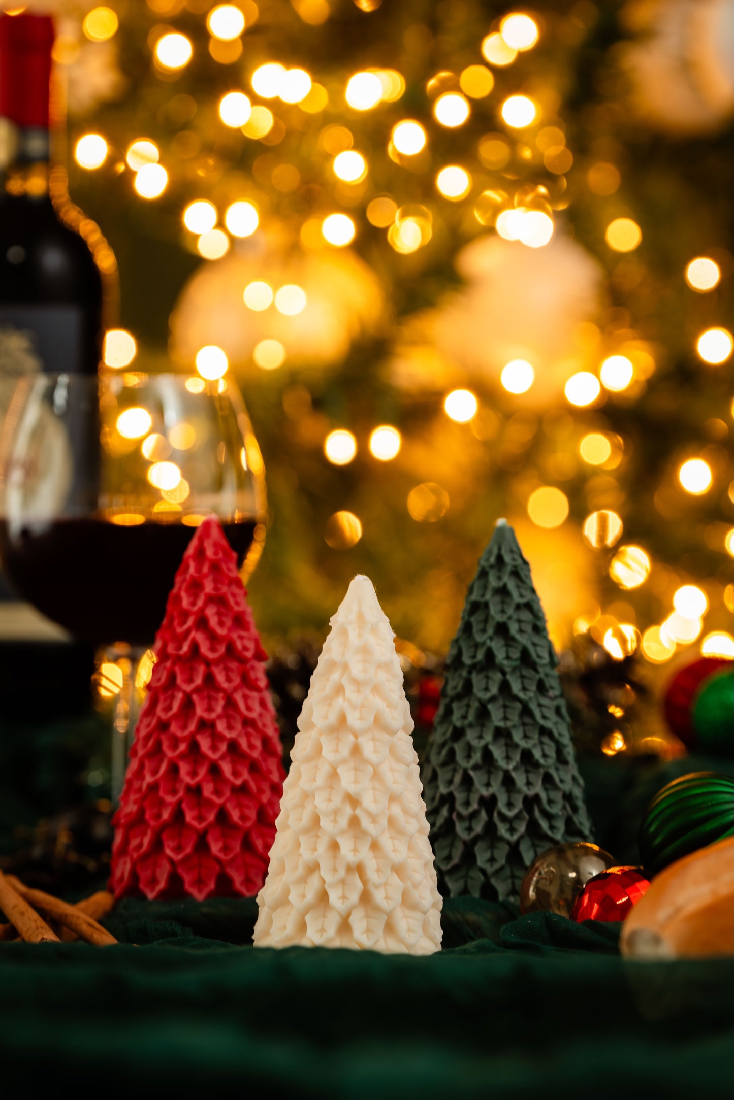 Three Christmas tree-shaped candles in red, white, and green with blurred lights in the background.