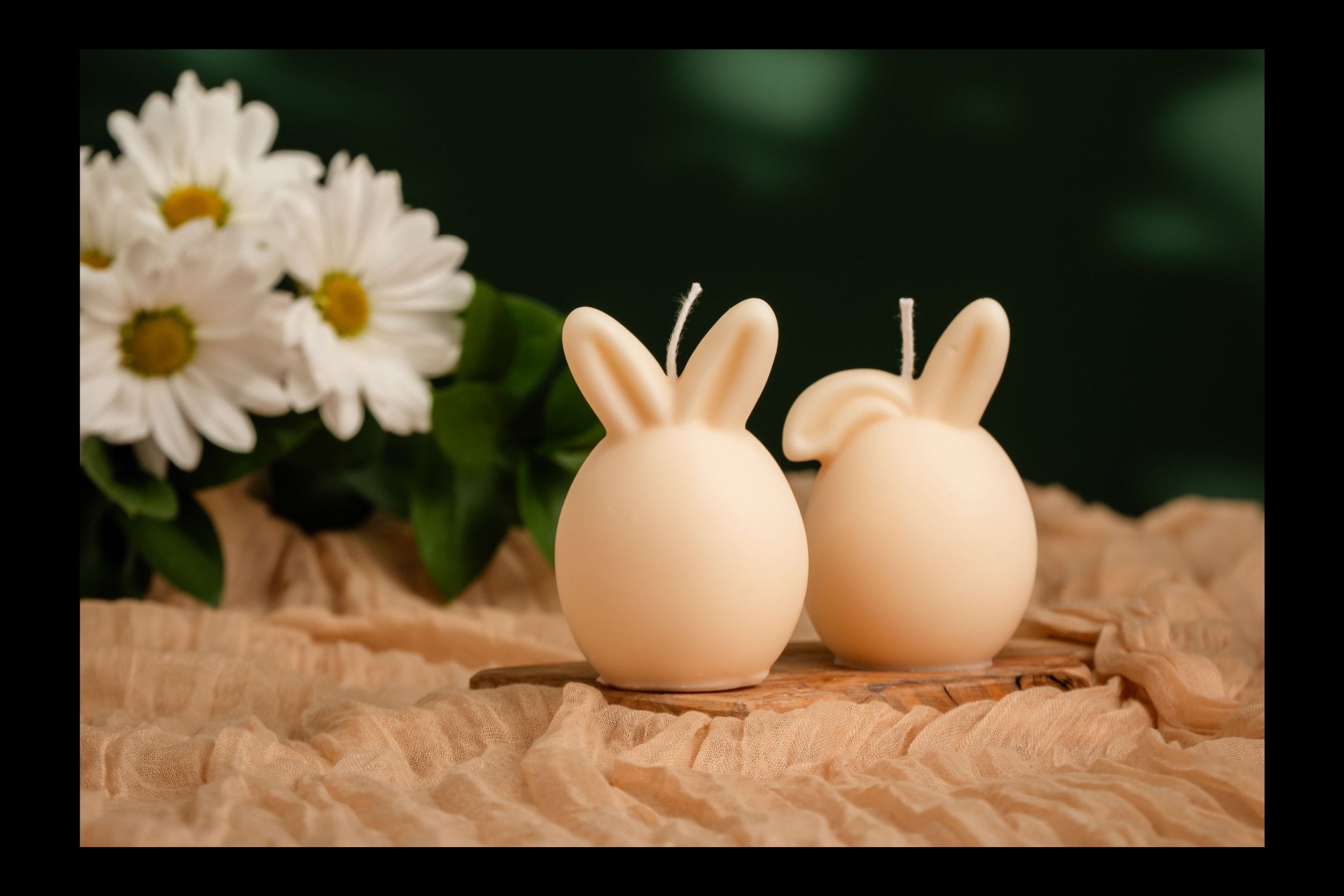 Two rabbit-shaped egg candles on a textured surface with a dark green leafy background