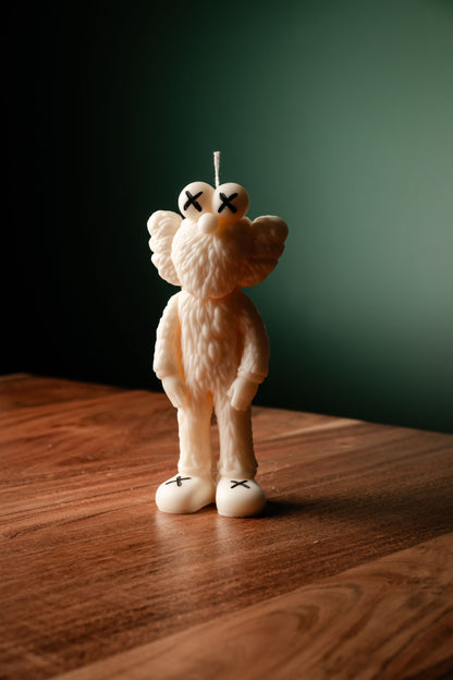 A decorative candle with a character design resembling a bear from Sesame Street, placed on a wooden surface with a dark background.