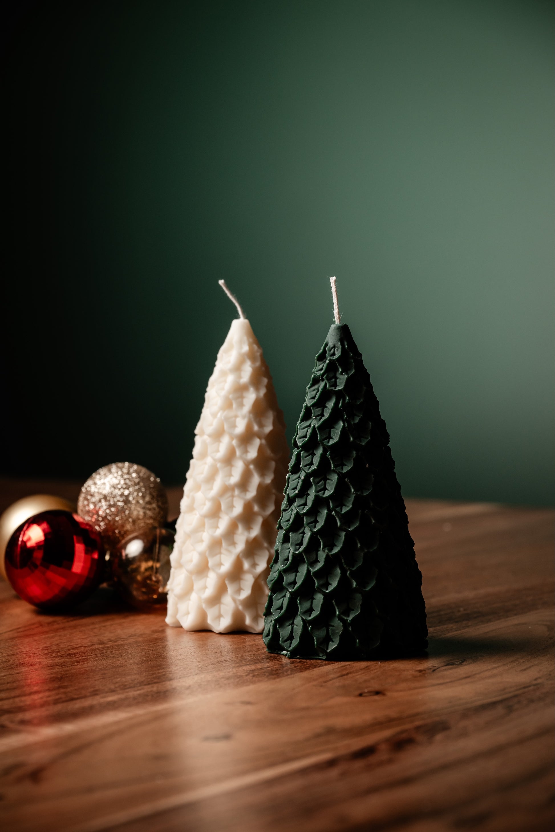 Two tree-shaped candles, one white and one green, on a wooden surface with a dark background.