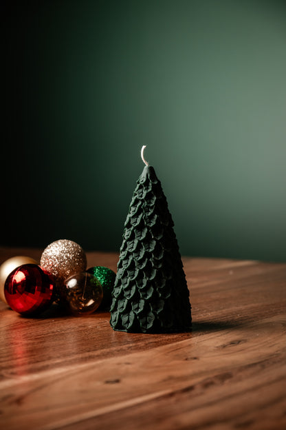 Green textured candle shaped like a Christmas tree on a wooden surface with decorative balls.