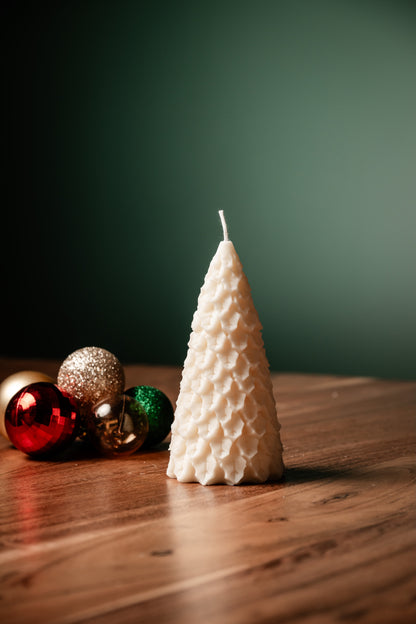Decorative candle shaped like a Christmas tree on a wooden surface with colorful ornaments.