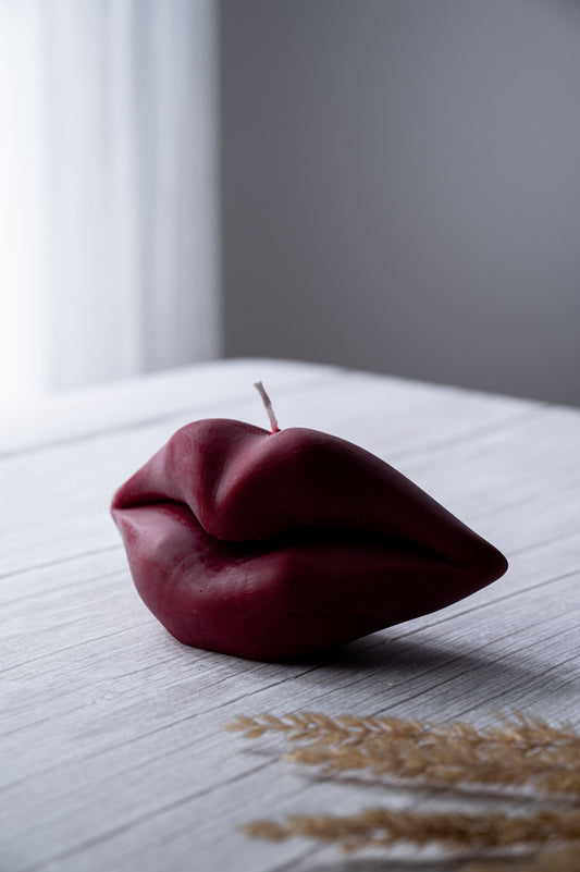 A lip-shaped, red candle on a white surface, with a blurred background.